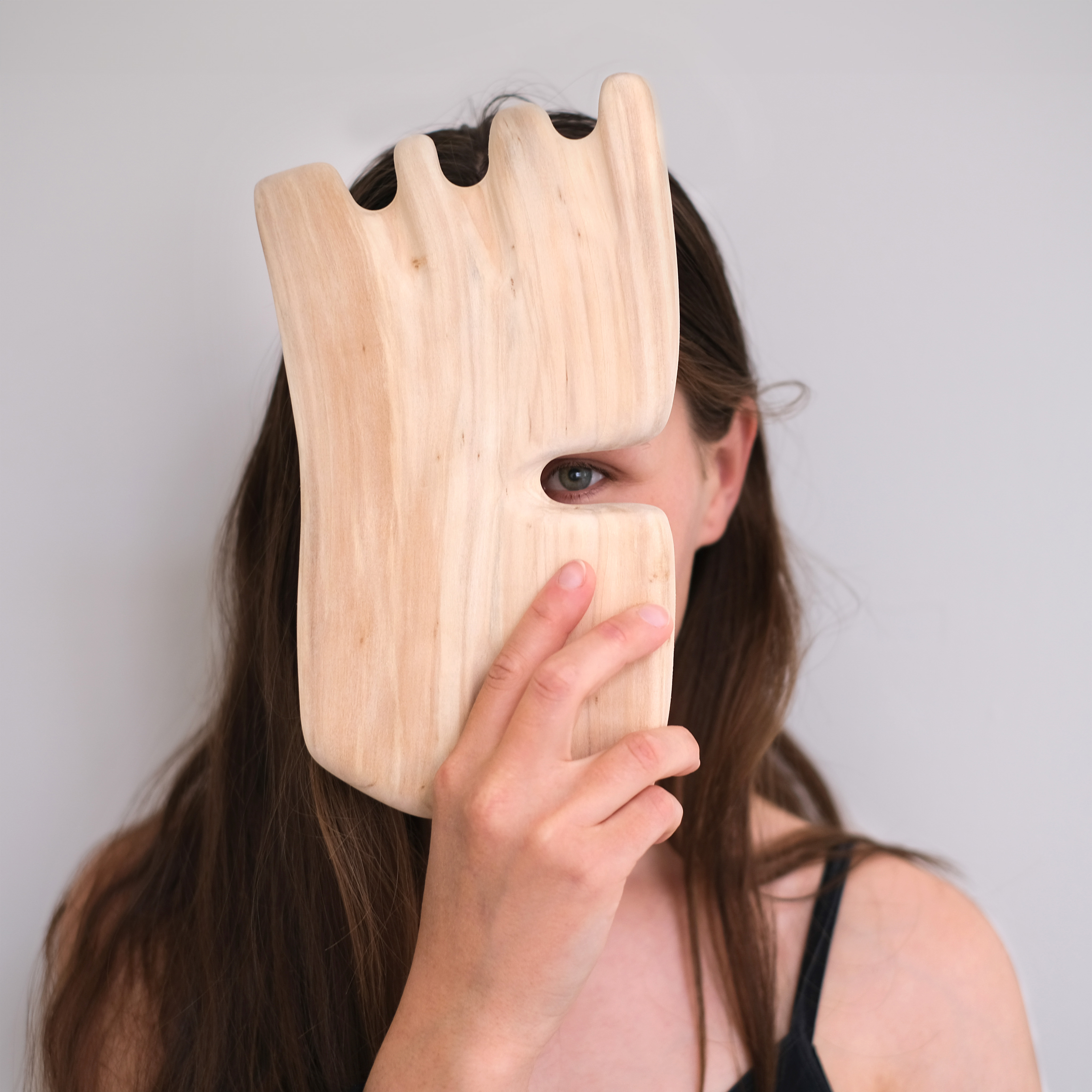 Portrait of an artist, Klára Čermáková, covering most of her face with one of her artifacts. A wooden organic object whose shape could remind you of a mask.