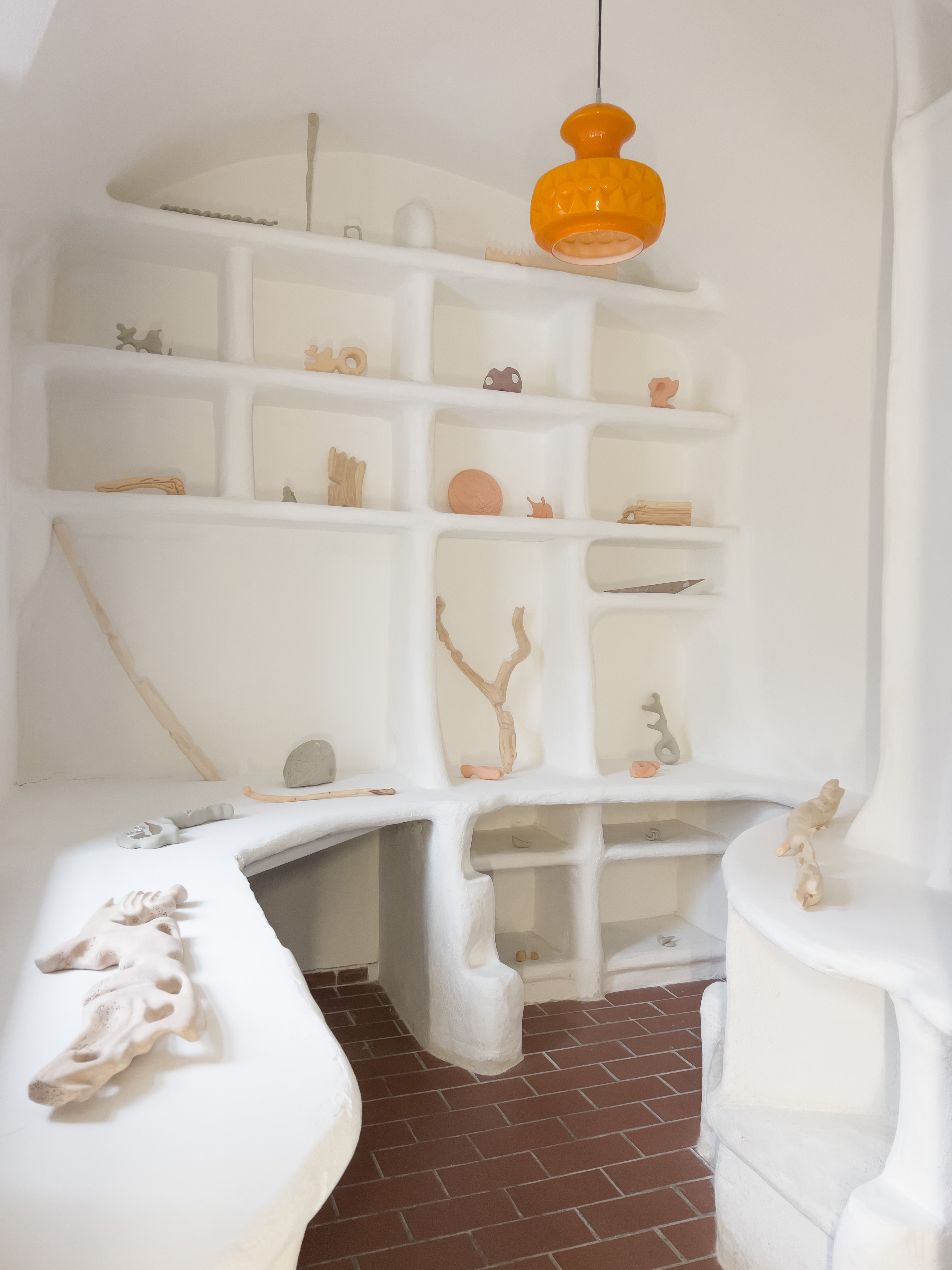 Photo of an art installation called Hands (and Other Products of Labor) 2.0 by Klára Čermáková (Common Space, Altes Spital, Viechtach, Germany) [Front view]. Several smaller art objects are displayed on organically shaped white shelves, initially serving as Pharmacy storage inside a small city hospital.