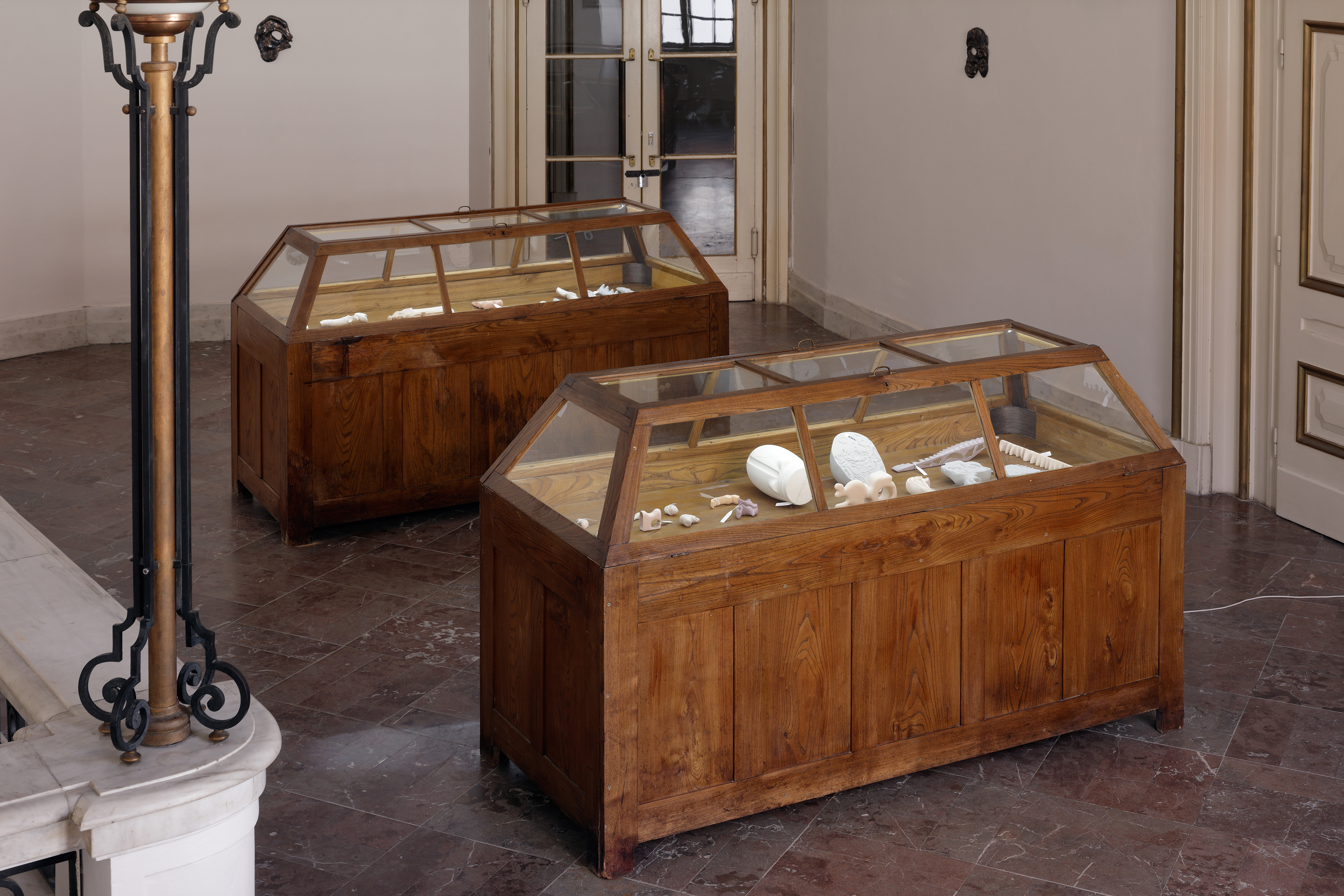 Photo of an art installation called Hands (and Other Products of Labor) 2.0 by Klára Čermáková (Mikulov Art Symposium, Mikulov, Czechia, 2021) [Front view]. There are several smaller art objects in two pieces of old museum furniture (called “coffins” for their unique shape).