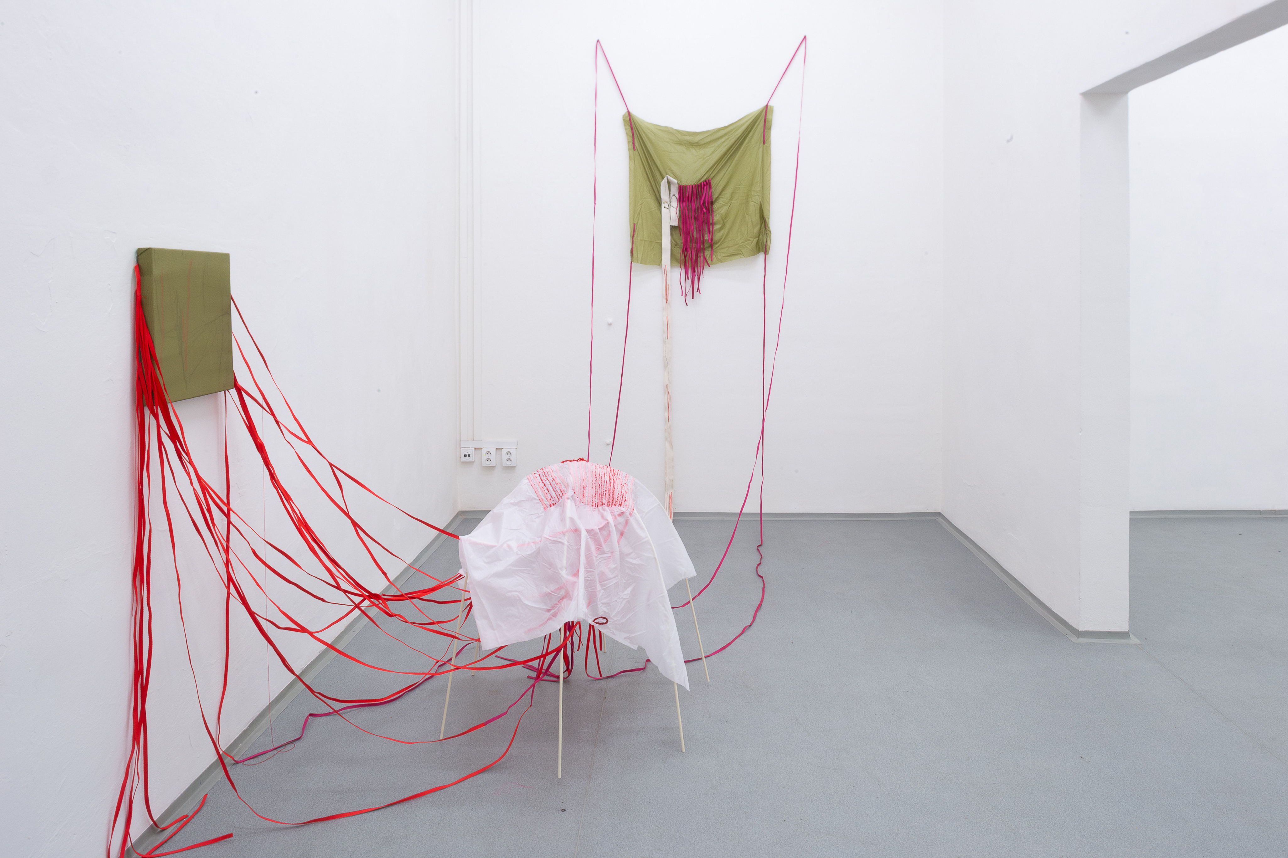 Photo of an art installation called Hands (and Other Products of Labor) 2.0 by Klára Čermáková (Mikulov Art Symposium, Mikulov, Czechia, 2021) [View on the back room 2]. A view into the back room shows a smaller metal skeleton covered in fabric loosely connecting to the stitched paintings hanging on the walls.